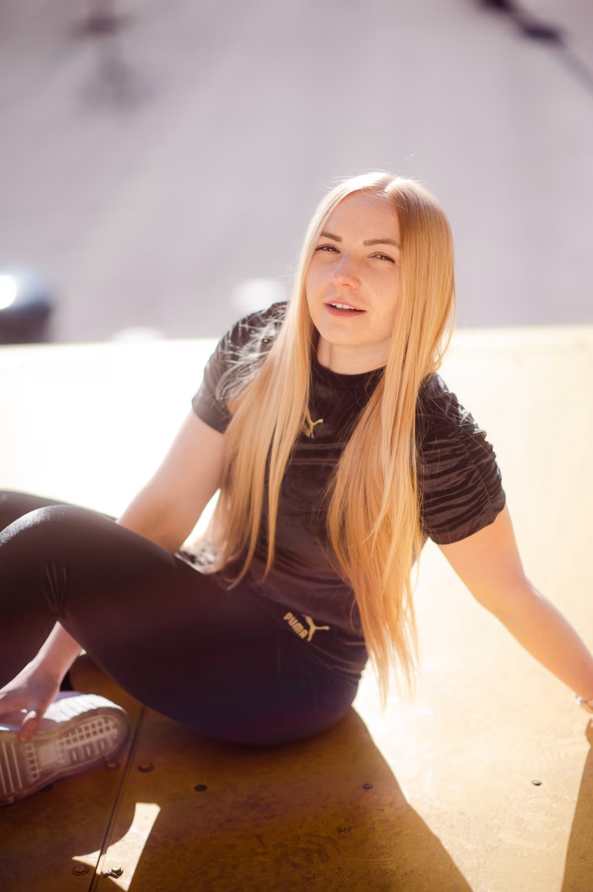 Woman sitting on a wooden floor wearing a brown t-shirt with a logo.